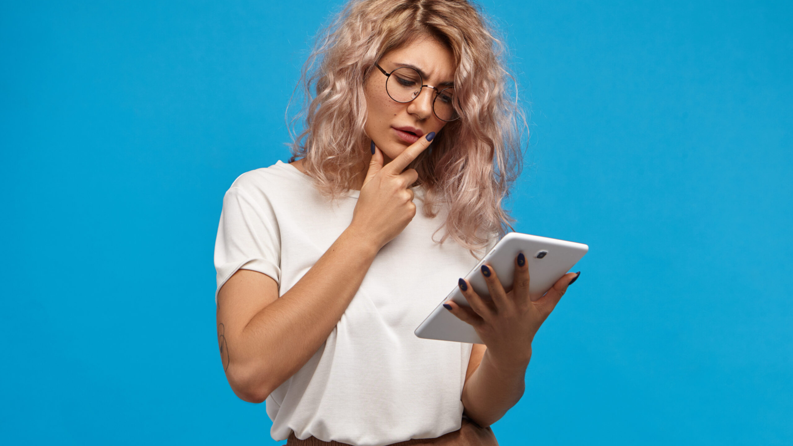 Thoughtful young attractive woman surfing internet reading world news or checking email on digital tablet. Pensive cute girl in eyewear using generic touch pad portable computer for remote work